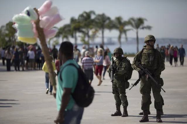 Soldiers stand guard in Maua square where a cotton candy vendor passes by in Rio de Janeiro, Brazil, Saturday, July 9, 2016, as security is deployed to get to know the areas they'll be patrolling during the Olympics. Roughly twice the security contingent at the London Olympics will be deployed during the August games in Rio, which are expected to draw thousands of foreigners to a city where armed muggings, stray bullets and turf wars between heavily armed drug gangs are routine. (Photo by Leo Correa/AP Photo)