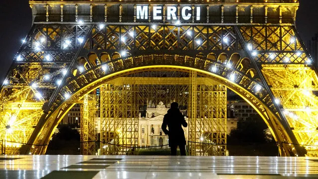 A man walks in front of Eiffel Tower lit up with the message “Merci” or “Thank you” in show of thanks to health workers battling the coronavirus pandemic in Paris, on April 2, 2020, on the seventeenth day of a lockdown in France to stop the spread of the novel coronavirus COVID-19. (Photo by Stefano Rellandini/AFP Photo)