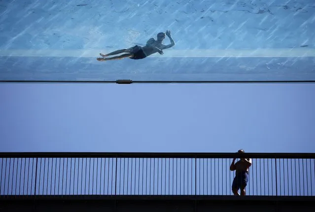 A person swims at the Embassy Gardens Sky Pool, a transparent acrylic swimming pool suspended between two apartment buildings, during hot weather in London, Britain, July 10, 2022. (Photo by Henry Nicholls/Reuters)