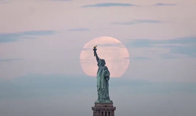 May's full Moon, known as the Full Flower Moon and is the last supermoon of the year, sets behind the Statue of Liberty on May 7, 2020 in New York City. (Photo by Johannes Eisele/AFP Photo)