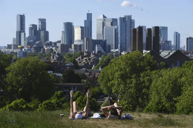 People sunbathe on the grass and enjoy the hot weather in Greenwich Park in London, backdropped by the City of London buildings, after the introduction of measures to slowly bring the country out of lockdown, Tuesday May 19, 2020.  The highly contagious COVID-19 coronavirus has impacted on nations around the globe, many imposing self isolation and exercising social distancing when people move from their homes. (Photo by Kirsty O'Connor/PA Wire via AP Photo)