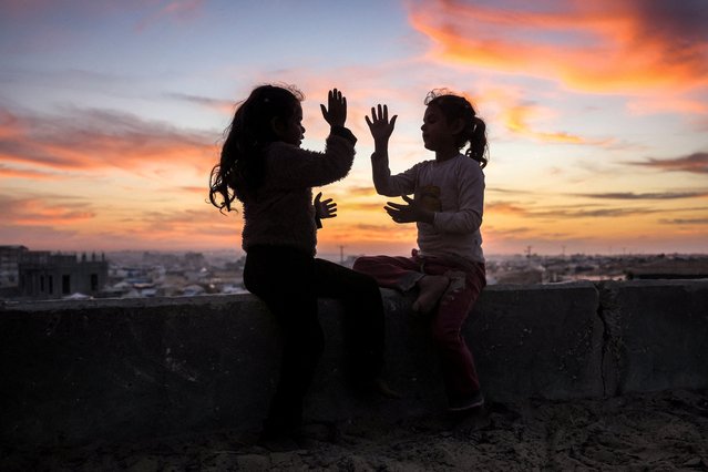 Two girls play together at sunset atop a concrete water storage tank overlooking the Hamad Residential City complex in the north of Khan Yunis in the southern Gaza Strip on December 22, 2024 amid the ongoing war in the Palestinian territory between Israel and Hamas. (Photo by Bashar Taleb/AFP Photo)