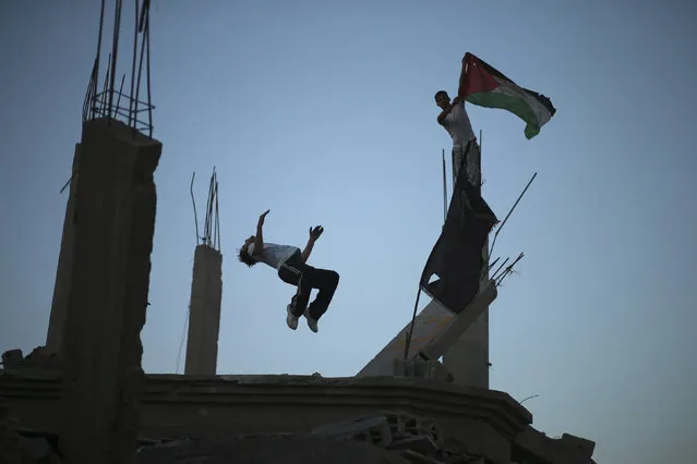 A Palestinian youth holds a Palestinian flag as his another practices Parkour skills over the ruins of house, which witnesses said was destroyed during a seven-week Israeli offensive, in the Shejaia neighborhood east of Gaza City October 1, 2014. (Photo by Mohammed Salem/Reuters)