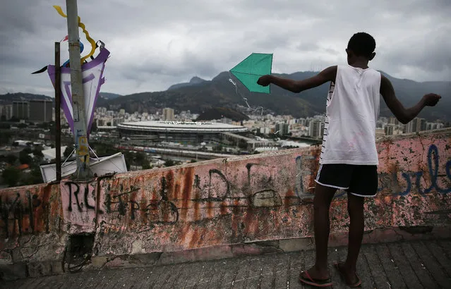 A teen prepares to fly a kite in the Mangueira “favela” community, with Maracana stadium in the background, on Day 5 of the Rio 2016 Olympic Games on August 10, 2016 in Rio de Janeiro, Brazil. Much of the Mangueira “favela” community sits about a kilometer away from Maracana stadium, the site of the opening and closing ceremonies for the Games. (Photo by Mario Tama/Getty Images)