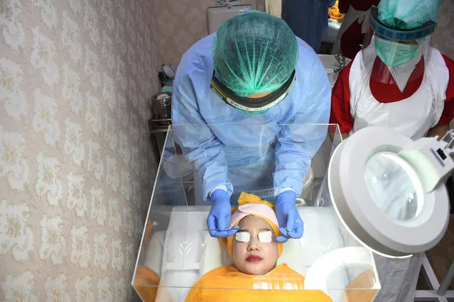 A patient performs treatment inside a protective acrylic box that is used as a preventative measure against a new coronavirus outbreak at a beauty clinic at Tambak Hospital in Jakarta, Indonesia, on June, 25,2020. Since the pandemic, several beauty and health clinics have implemented health protocols to protect patients from being prevented from transmitting the corona virus. (Photo by Dasril Roszandi/NurPhoto via Getty Images)