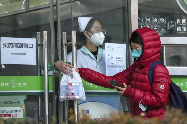 A woman collects COVID-19 antigen kits from a worker at a pharmacy in Beijing, Sunday, December 11, 2022. (Photo by Andy Wong/AP Photo)