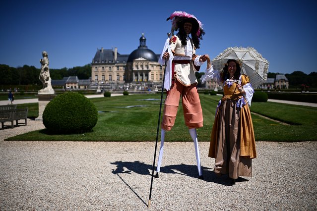A man on stilt and a woman dressed in 17th-century costumes pose as they take part in “La grande journee des costumés”, an historical event gathering hundreds at the Vaux-le-Vicomte castle (background) in Maincy, some 50 kms south-east of Paris on June 25, 2023. (Photo by Christophe Archambault/AFP Photo)