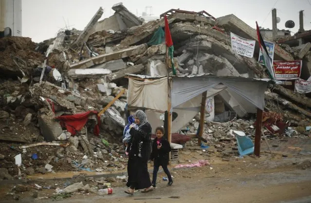A Palestinian woman holding her child walks past the ruins of a house that witnesses said was destroyed by Israeli shelling during the most recent conflict between Israel and Hamas, on a rainy day in the east of Gaza City November 16, 2014. (Photo by Suhaib Salem/Reuters)