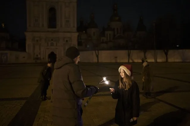A girl lights a sparkler in Sophia Square before curfew on New Year's Eve in Kyiv, Ukraine, Saturday, December 31, 2022. Multiple blasts rocked the capital and other areas of Ukraine on Saturday. (Photo by Felipe Dana/AP Photo)