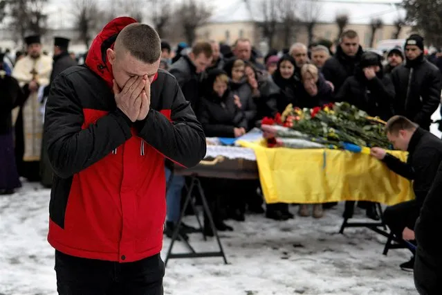 A friend reacts next to a coffin with the body of Ukrainian decathlete and serviceman Volodymyr Androshchuk, who was recently killed in a fight against Russian troops near the Bakhmut town, amid Russia's attack on Ukraine, during a funeral ceremony in the town of Letychiv, Khmelnytskyi region, Ukraine on February 1, 2023. (Photo by Valentyn Ogirenko/Reuters)