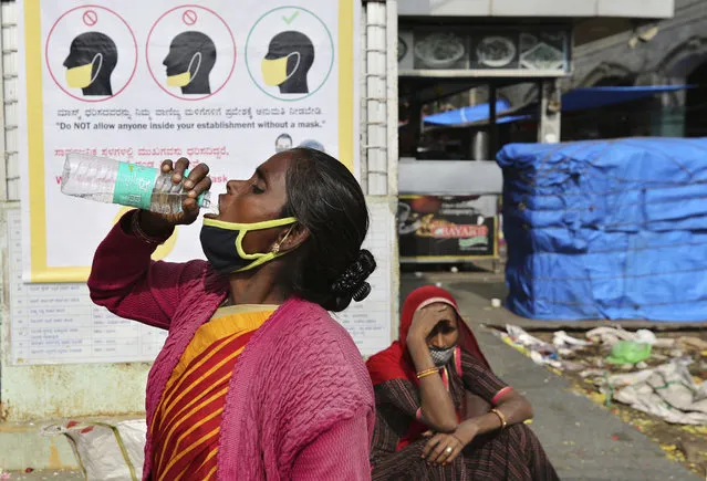 An Indian woman removes her face mask to drink water next to a poster displaying appropriate use of masks at a market in Bengaluru, India, Thursday, October 29, 2020. India's confirmed coronavirus caseload surpassed 8 million on Thursday with daily infections dipping to the lowest level this week, as concerns grew over a major Hindu festival season and winter setting in. (Photo by Aijaz Rahi/AP Photo)