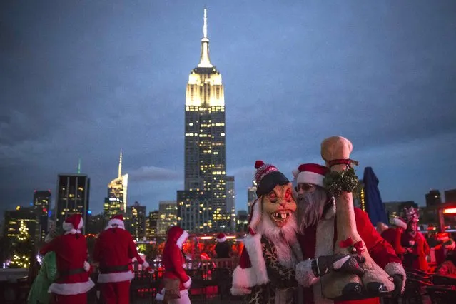 The Empire State Building is seen in the background as revelers taking part in SantaCon are pictured at a top a rooftop bar after sunset in Midtown Manhattan, New York  December 13, 2014. (Photo by Elizabeth Shafiroff/Reuters)