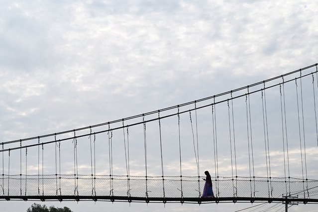 A woman checks her mobile phone as she walks on a footbridge in Lalitpur, Nepal, on September 19, 2025. (Photo by Monika Malla/Reuters)