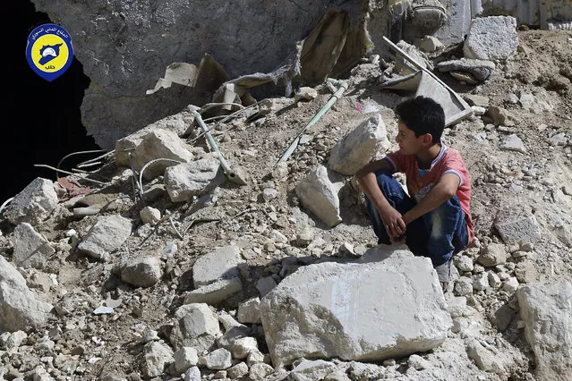 In this picture taken, Tuesday, October 11, 2016, provided by the Syrian Civil Defense group known as the White Helmets, a boy sits amongst rubble in rebel-held eastern Aleppo, Syria. Activists and rescue workers say an intensive day of bombing on besieged rebel-held parts of Aleppo has left at least 25 people dead, including five children. Rescue workers pulled at least one boy alive from under the rubble late Tuesday night. The Britain-based Syrian Observatory for Human Rights says Wednesday that Tuesday's bombings killed 25 people. The Syrian Civil Defense, a team of first responders, and activist media platform Aleppo Media Center put the death toll at 41. (Photo by Syrian Civil Defense- White Helmets via AP Photo)