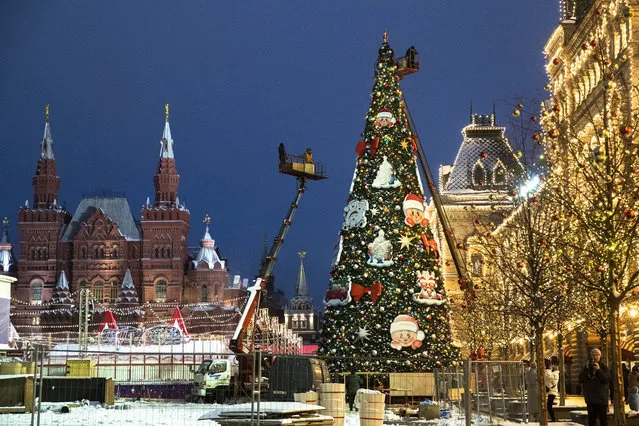 Municipal workers on cranes set up a Christmas tree in Red Square, with the Historical Museum, left, and the GUM State Department store, right, in the background, in Moscow, Russia, Monday, November 23, 2020. Daily new coronavirus infections in Russia hit a new high on Monday, with authorities reporting a record 25,173 new cases. The latest figure brings the country's total to over 2.1 million. (Photo by Pavel Golovkin/AP Photo)