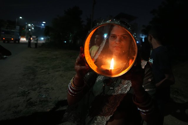 An Indian Hindu married woman looks at the moon through a sieve as part of a ritual to break her fast during Karva Chauth festival, in Ahmedabad, India, Friday, October 10, 2025. (Photo by Ajit Solanki/AP Photo)