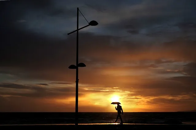 A man with an umbrella walks during rain as the sun sets in Ayia Napa resort in the eastern Mediterranean island of Cyprus, Sunday, December 31, 2017. (Photo by Petros Karadjias/AP Photo)