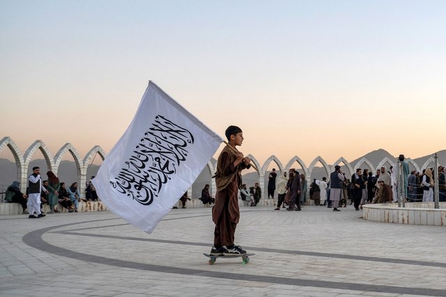 An Afghan boy carries the Taliban flag as he skates across the Wazir Akbar Khan hilltop in Kabul on October 13, 2025. (Photo by Wakil Kohsar/AFP Photo)