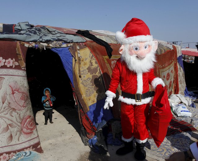 A volunteer wearing a Santa Claus costume distributes presents to children at a poor community in Najaf, south of Baghdad, December 19, 2015. (Photo by Alaa Al-Marjani/Reuters)