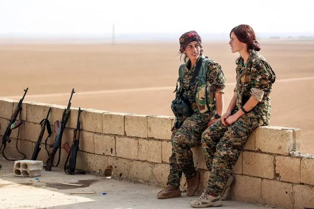 Shirin (L) and Kazîwar (R), members of the Kurdish female Women's Protection Units (YPJ) engage in conversation next to Kalashnikov assault rifles on a house rooftop in the Syrian village of Mazraat Khaled, some 40 kms away from the Islamic State group's (IS) de-facto capital of Raqa on November 9, 2016. (Photo by Delil Souleiman/AFP Photo)