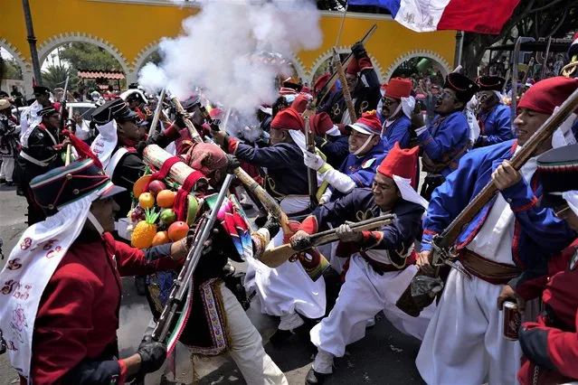 People dressed as Zacapoaxtla Indigenous soldiers clash with others playing the part of French soldiers as they reenact The Battle of Puebla as part of Cinco de Mayo celebrations in the Peñon de los Baños neighborhood of Mexico City, Thursday, May 5, 2022. Cinco de Mayo commemorates the victory of an ill-equipped Mexican army over French troops in Puebla on May 5, 1862. (Photo by Eduardo Verdugo/AP Photo)