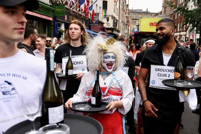 People wait at the start line of the waiters race at the Soho Village Fete in London, Britain on July 16, 2023. The race was delayed when a fire engine arrived to tackle a fire in a shop next to the start line. (Photo by Kevin Coombs/Reuters)