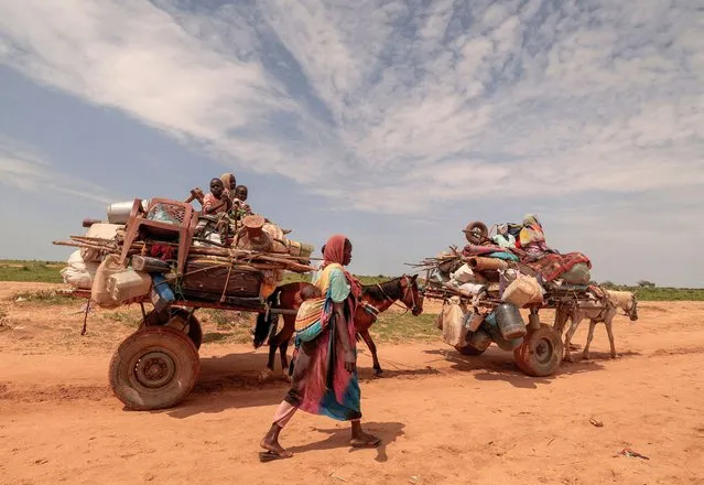 A Sudanese woman, who fled the conflict in Murnei in Sudan's Darfur region, walks beside carts carrying her family belongings upon crossing the border between Sudan and Chad in Adre, Chad on August 2, 2023. (Photo by Zohra Bensemra/Reuters)
