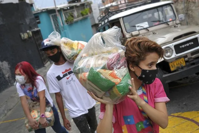 Youth carry bags of basic food staples, such as pasta, sugar, flour and kitchen oil, provided by a government food assistance program, to delivery it in the Santa Rosalia neighborhood of Caracas, Venezuela, Saturday, April 10, 2021. (Photo by Matias Delacroix/AP Photo)