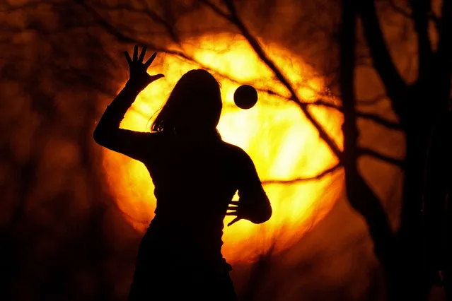 A girl is silhouetted against the setting sun she plays a game with friends on a spring-like day Saturday, March 6, 2021, in Kansas City, Mo. (Photo by Charlie Riedel/AP Photo)