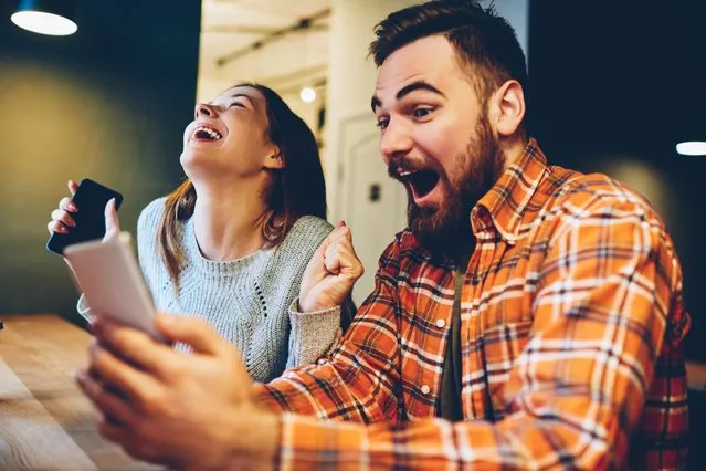 Excited male and female hipsters rejoice in winning an internet lottery made bets on website on modern smartphone.Happy couple in love celebrating victory in online competitions enjoying success. (Photo by GaudiLab/Getty Images)