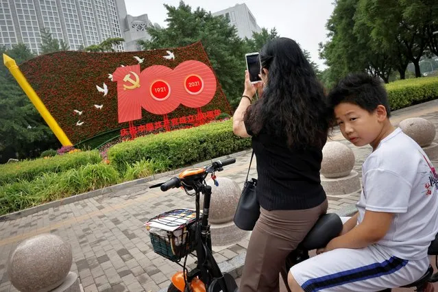 A woman takes pictures of a flower arrangement marking the upcoming 100th founding anniversary of the Communist Party of China in Beijing on June 26, 2021. (Photo by Thomas Peter/Reuters)
