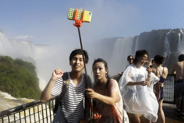 In this Saturday, March 14, 2015 photo, Japanese tourists Hiromi Kanetake, right, and her son Takayuki, photograph themselves with a phone camera as they stand in the spray on the Brazilian side of Iguazu falls, behind, in Foz do Iguazu, Brazil. Iguazu Falls is located on Brazil's border with Argentina. (Photo by Jorge Saenz/AP Photo)