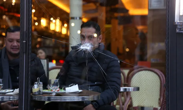 Men sit in a bar behind a damaged window on the Champs- Elysees avenue in Paris on November 25, 2018 after a rally by yellow vest (Gilets jaunes) protestors against rising oil prices and living costs. Security forces in Paris fired tear gas and water cannon on November 24 to disperse protesters. Several thousand demonstrators, wearing high- visibility yellow jackets, had gathered on the avenue as part of protests which began on November 17, 2018. (Photo by Zakaria Abdelkafi/AFP Photo)