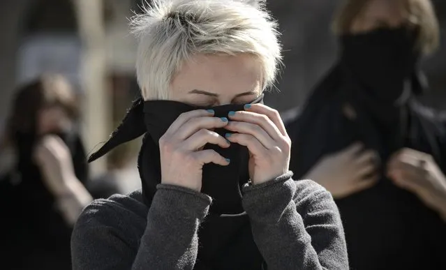 A woman covers her face with a black scarf during a performance honoring the history of feminist movements, marking the International Women's Day in Bucharest, Romania, Tuesday, March 8, 2016. (Photo by Andreea Alexandru/AP Photo)