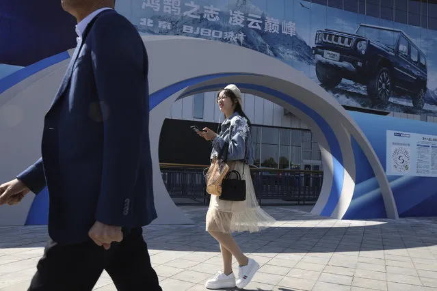A woman walks past the entrance to the Auto Shanghai 2019 show in Shanghai on Monday, April 15, 2019. This year's Shanghai auto show which starts Thursday highlights the global industry's race to make electric cars Chinese drivers want to buy as Beijing winds down subsidies that promoted sales. (Photo by Ng Han Guan/AP Photo)