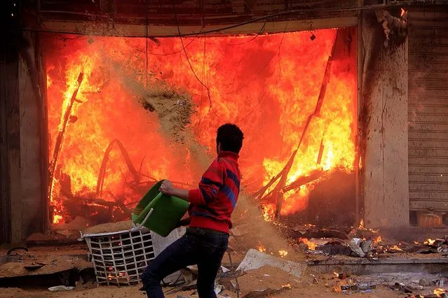 A civilian tries to put out a fire started by Muslim Brotherhood supporters during clashes near the Giza Pyramids, in Giza, on March 14, 2014. Supporters of Egypt's ousted president, who hails from the Muslim Brotherhood, set fire to a clothing shop during clashes with Morsi opponents. (Photo by Hamada Elrasam/Associated Press)