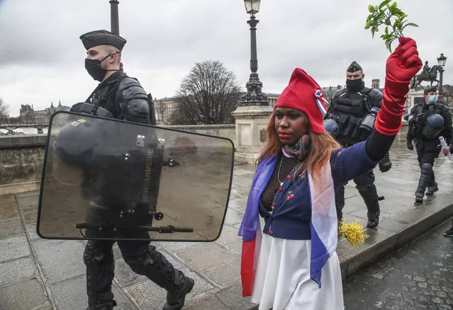 A protester dressed as Marianne, the symbol of the French Republic since the 1789 revolution walks next to riot police officers during a march for freedom in Paris, Saturday, January 23, 2021. Hundreds of demonstrators marched on France's parliament Saturday protesting layoffs related to the virus crisis and demanding the resignation of the government. (Photo by Michel Euler/AP Photo)