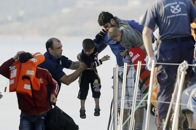 A father gives his son to a coast guard officer, second left, as he disembarks from a vessel at the port of Mitylene after being picked up by the Greek coast guard near the northeast Greek island of Lesvos on Wednesday, June 17, 2015. Around 100,000 migrants have entered Europe so far this year as Italy and Greece have borne the brunt of the surge with many more migrants expected to arrive from June through to September. (AP Photo/Thanassis Stavrakis)