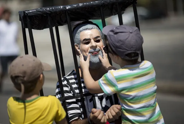 A man impersonating former president Luiz Inacio Lula da Silva in prison stripes is touched by a boy during a protest against corruption at Copacabana beach, in Rio de Janeiro, Brazil, Sunday, March 26, 2017. The protest come at a time when the so-called Car Wash investigation into billions of dollars in kickbacks expands to several Latin American countries. (Photo by Silvia Izquierdo/AP Photo)