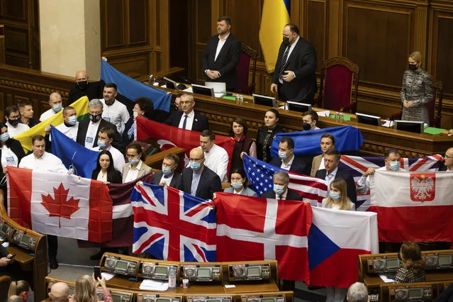 Ukrainian lawmakers hold state flags of Ukraine's partners to show their appreciation of political support and military aid during a session of parliament in Kyiv, Ukraine, Tuesday, February 1, 2022. (Photo by Mikhail Palinchak/AP Photo)