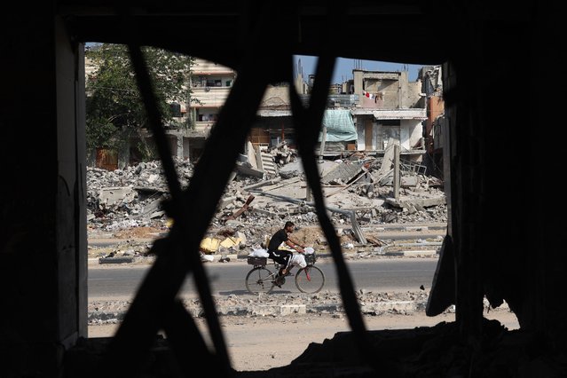 A Palestinian man rides a bicycle past damaged buildings after an overnight Israeli strike in al-Bureij camp in the central Gaza Strip on June 3, 2024, amid the ongoing conflict between Israel and the Palestinian Hamas militant group. (Photo by Eyad Baba/AFP Photo)