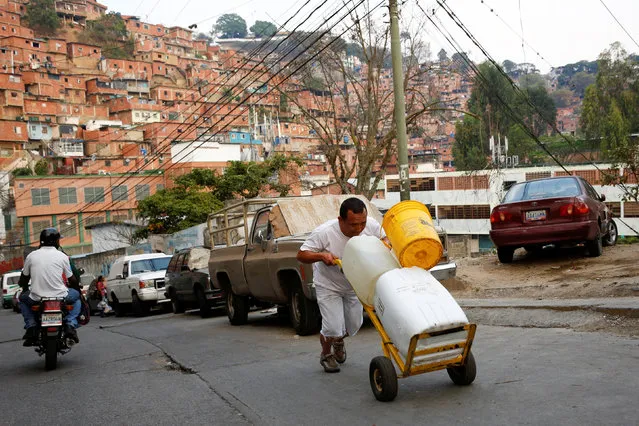 A man pushes a wheelbarrow loaded with water containers in a neighbourhood called “The Tank” at the slum of Petare in Caracas, Venezuela, March 17, 2016. (Photo by Carlos Garcia Rawlins/Reuters)