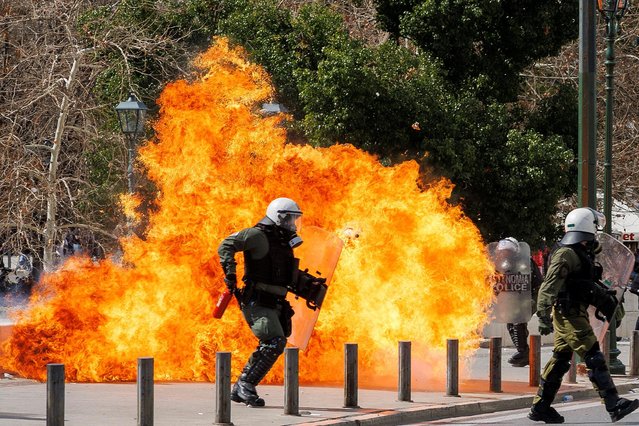 A riot police officer walks next to flames as clashes take place during a demonstration following the collision of two trains, near the city of Larissa, in Athens, Greece, March 5, 2023. (Photo by Alkis Konstantinidis/Reuters)