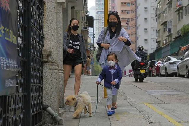 A child wearing a face mask walks a dog in Hong Kong, Sunday, March 13, 2022. The territory's leader, Chief Executive Carrie Lam, warned the peak of the latest surge in coronavirus infections might not have passed yet. (Photo by Kin Cheung/AP Photo)