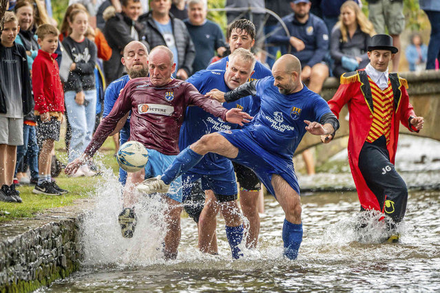 Footballers from Bourton Rovers fight for the ball in the River Windrush during the annual traditional river football match in the Cotswolds village of Bourton-in-the-Water, England, Monday, August 30, 2021. (Photo by Ben Birchall/PA Wire via AP Photo)
