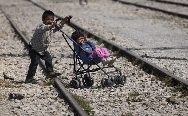 A boy pushes a stroller with a child at the migrants camp in Idomeni, Greece, Sunday, May 22, 2016.  Thousands of stranded refugees and migrants have camped in Idomeni for months after the border was closed. (Photo by Darko Bandic/AP Photo)