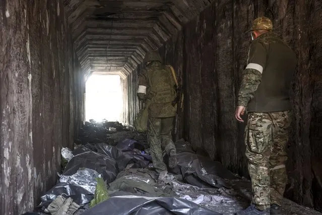 Servicemen of the Donetsk People's Republic militia look at bodies of Ukrainian soldiers placed in plastic bags in a tunnel, part of the Illich Iron & Steel Works Metallurgical Plant, the second largest metallurgical enterprise in Ukraine, in an area controlled by Russian-backed separatist forces in Mariupol, Ukraine, Monday, April 18, 2022. Mariupol, a strategic port on the Sea of Azov, has been besieged by Russian troops and forces from self-proclaimed separatist areas in eastern Ukraine for more than six weeks. (Photo by Alexei Alexandrov/AP Photo)