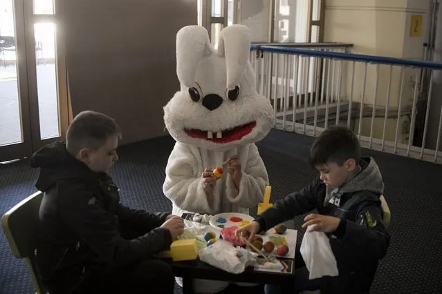 Children who fled the war from neighboring Ukraine paint Easter eggs next to an entertainer dressed in a rabbit costume during an event for Ukrainian refugee children on Maundy Thursday in a center for refugees in Bucharest, Romania, Thursday, April 21, 2022. Orthodox worshipers, which form the majority of Romanians, celebrate Easter Sunday, April 24. (Photo by Andreea Alexandru/AP Photo)