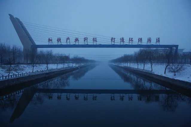 Morning mist rises from the canal that runs through the Guantao Chemical Industry Park near the village of East Luzhuang, Hebei province, February 22, 2017. The sign reads: “Speed up production upgrading. Create an environmentaly friendly industrial park”. (Photo by Thomas Peter/Reuters)