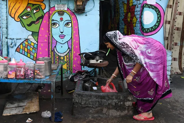 A woman collects water in front of a home adorned with a mural painted by artists from “Delhi Street Art” group at the Raghubir Nagar slum in New Delhi on December 2, 2019. (Photo by Sajjad Hussain/AFP Photo)